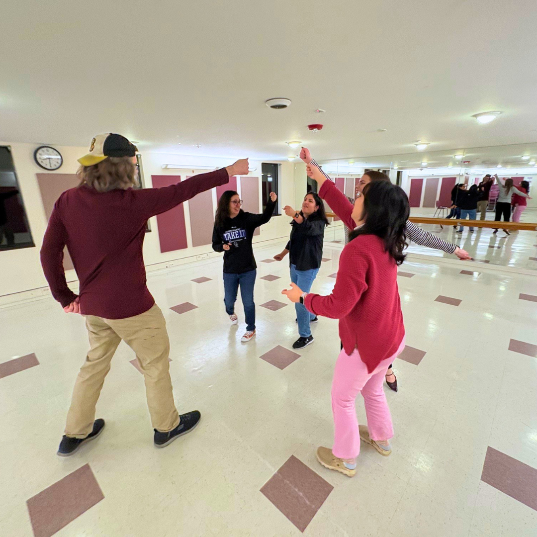 Improv classes with students gathered in a circle, reaching up high.